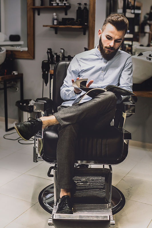 Cliente en peluquería Hombre sentado en sillón de barbería leyendo revista